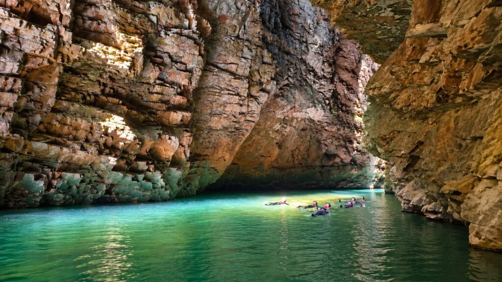 Grupo de visitantes realiza flutuação nas águas verde-esmeralda da Cachoeira do Dragão, entre imponentes paredões rochosos na Chapada dos Veadeiros, Goiás.