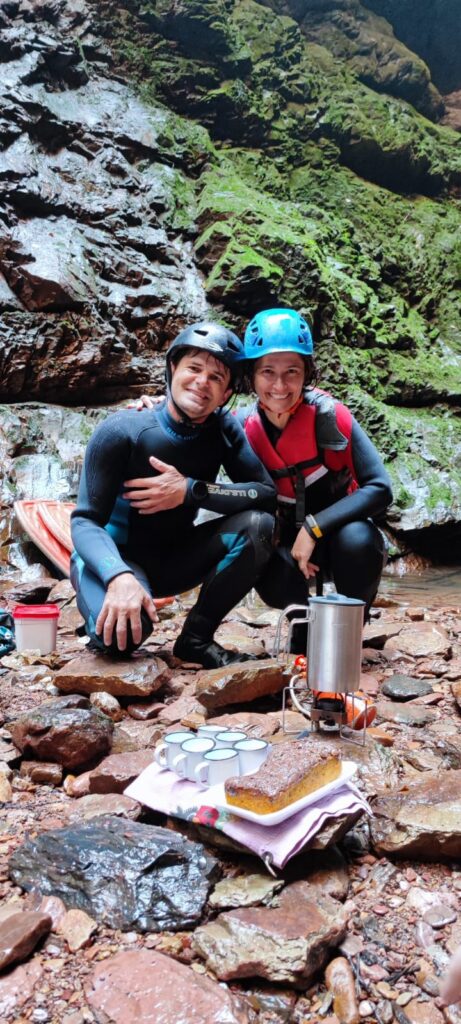Gudu e Milene com roupas de neoprene e capacetes se segurança preparando o cafézinho sobre pedras, cercados por paredões rochosos e vegetação na Cachoeira do Dragão na Chapada dos Veadeiros, Goiás, Brasil.