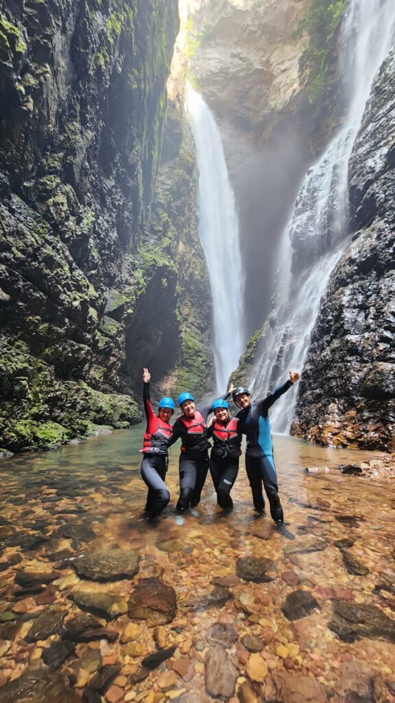 Milene, Suellen, Malu e Gudu, com roupas de neoprene, capacetes e coletes de segurança, posam nas águas rasas diante da imponente Cachoeira do Dragão, na Chapada dos Veadeiros.